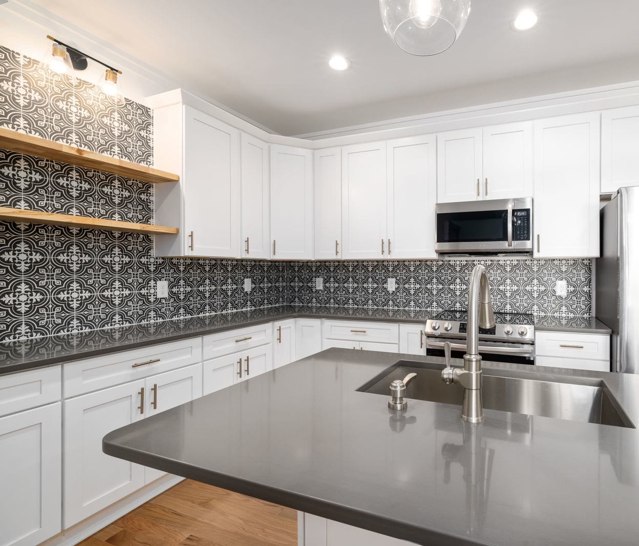 A white kitchen with a black and white patterned tile backsplash, open wood shelving and a stainless steel range