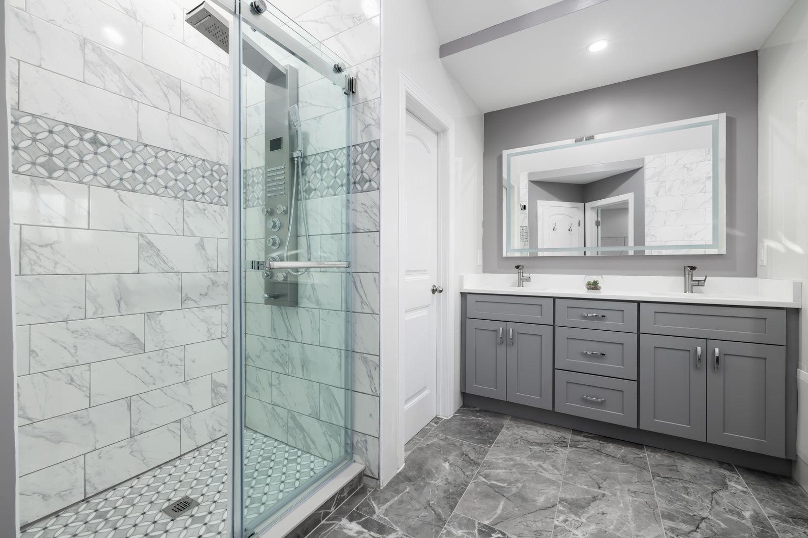 A remodelled bathroom with grey vanity cabinets and a marble-tiled walk-in shower