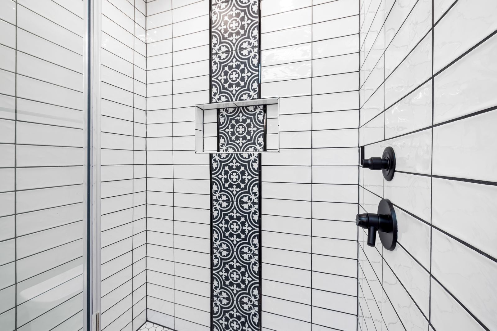 A walk-in shower tiled in white stacked tile with a patterned mosaic niche and matte black fixtures